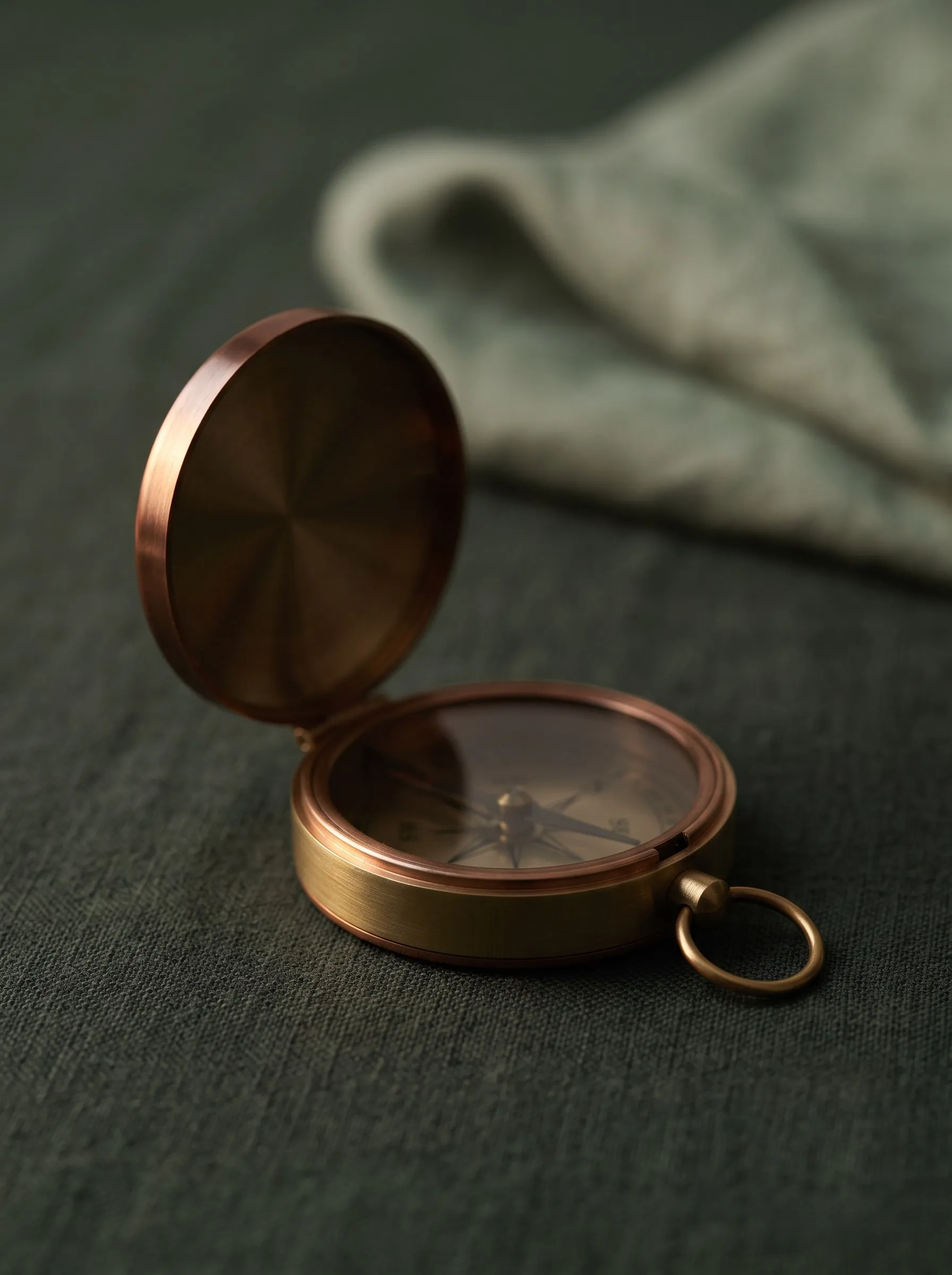 An open brass compass resting on green linen.