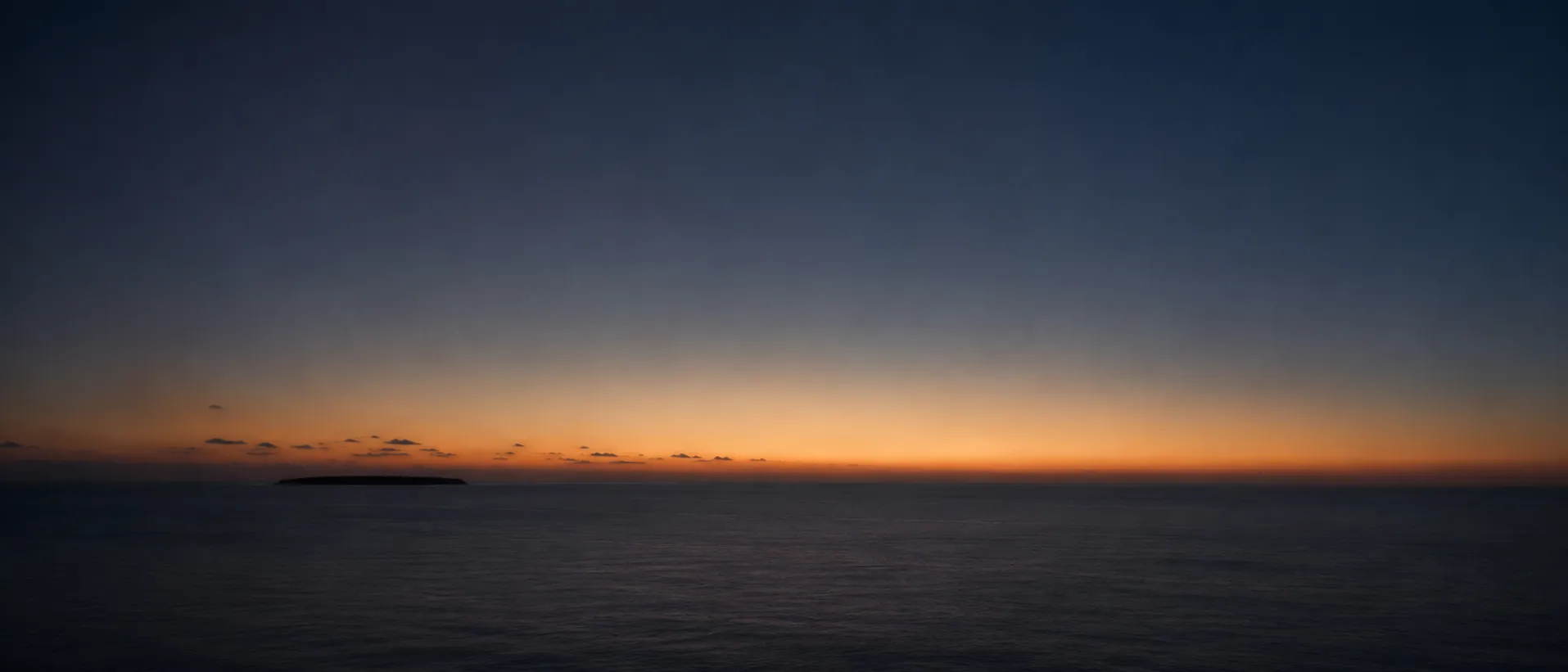 Last light over the ocean with a single distant island on the horizon.