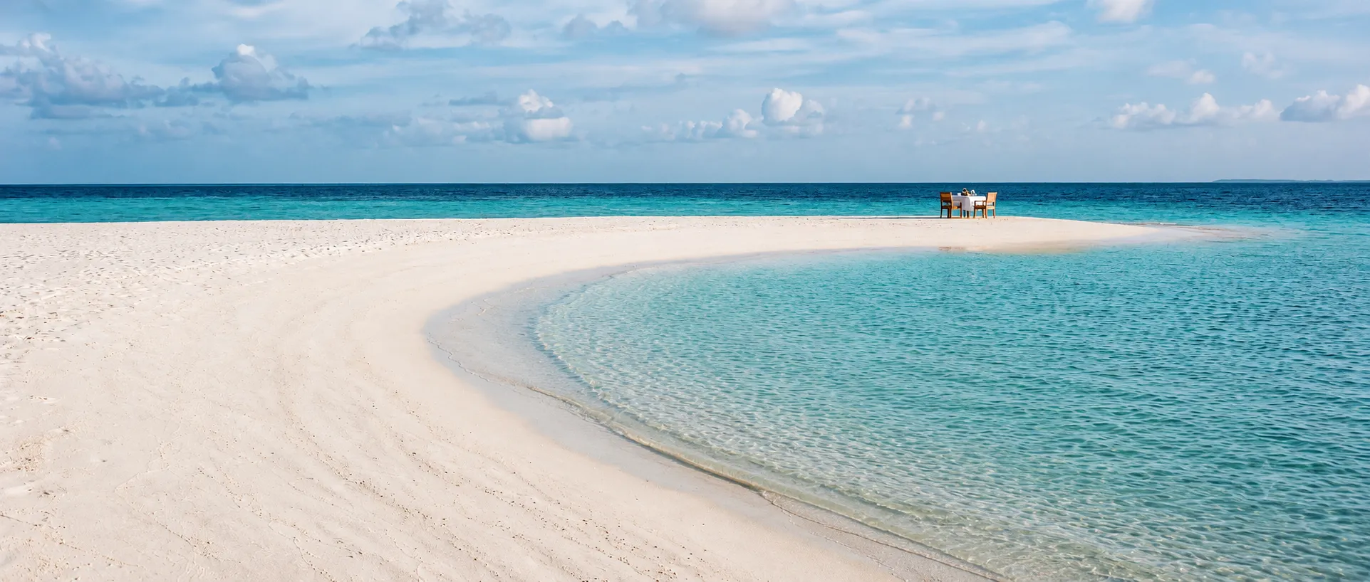 A white sandbank curving into turquoise water with a single table set at its tip.