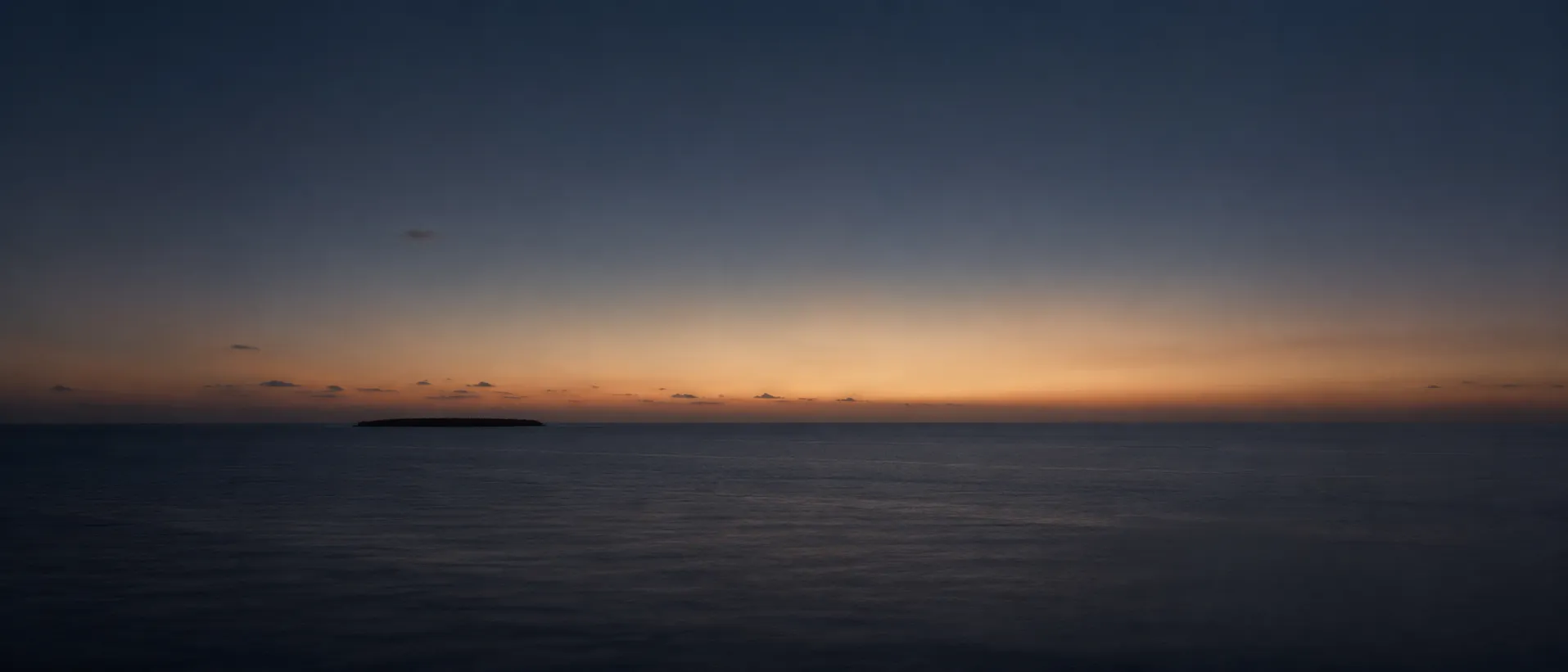 A single Maldivian island at dusk in a wide, darkening sea, the last light along the horizon.