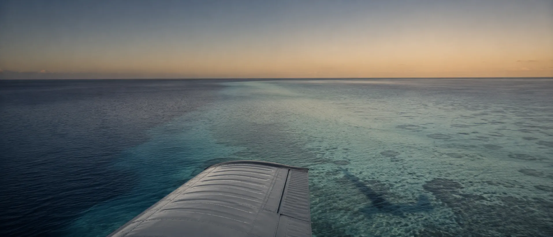 A seaplane wing over gradient lagoon water in late afternoon light.