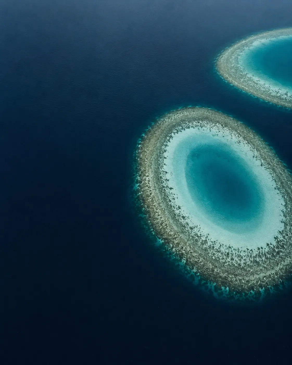 Atoll rings seen from above, deep blue water shading to pale lagoon.